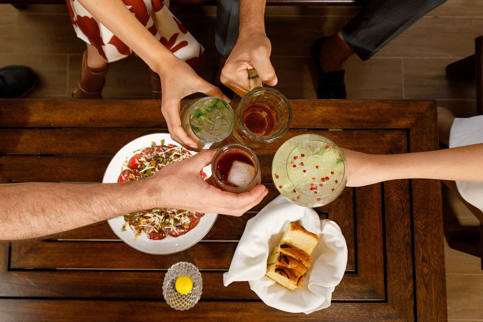 Cheers to Good Times Friends toasting with creative cocktails and sharing tapas at Bak'tun Lounge wooden table